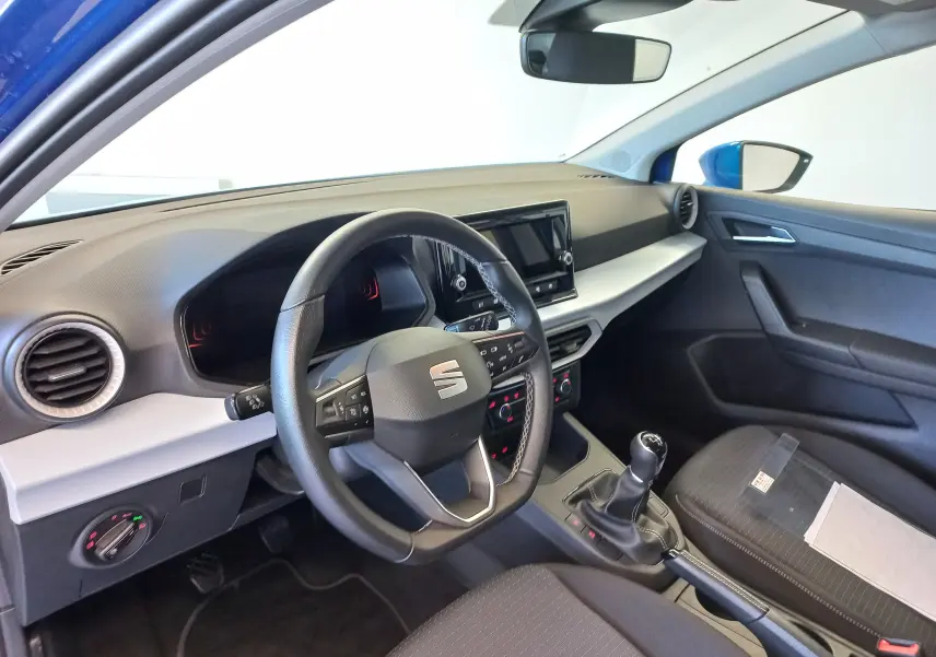 Vue intérieure côté conducteur du SEAT Ibiza 2025 bleu saphir, mettant en valeur le volant, la console centrale et la boîte manuelle.