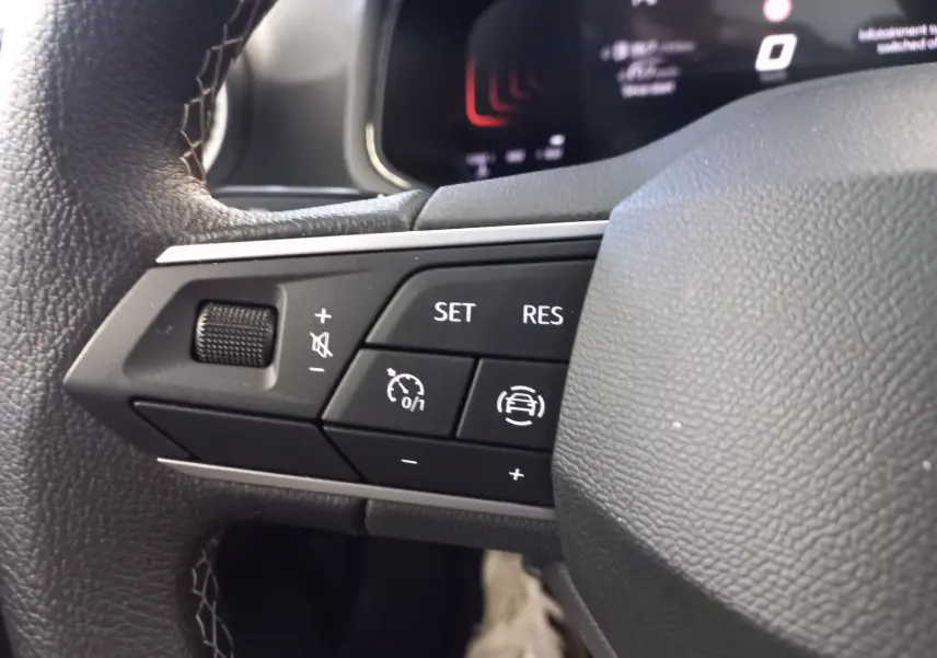Gros plan sur les commandes au volant côté gauche de la SEAT Ibiza 2025, avec boutons de régulateur et assistant de conduite.