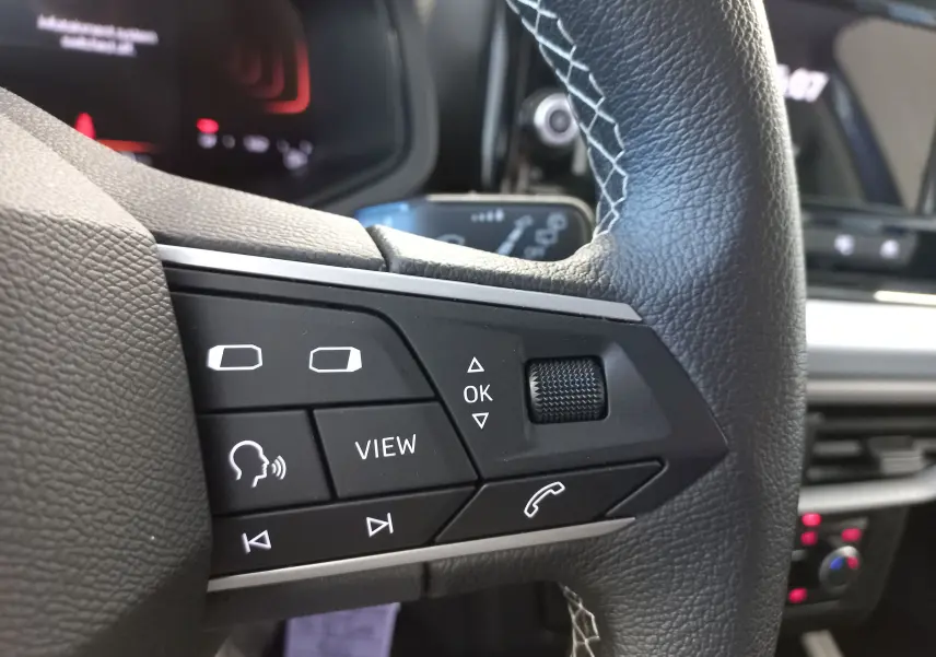 Gros plan sur les commandes gauche du volant en cuir noir du SEAT Ibiza 2025, avec boutons multifonctions et molette.