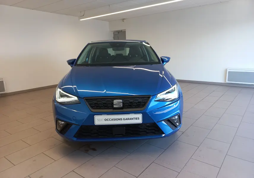 Vue avant d'une SEAT Ibiza 2025 bleu saphir avec phares allumés dans un showroom lumineux.