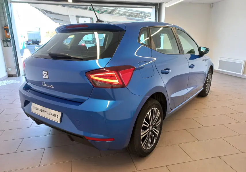 Vue 3/4 arrière droite d'une SEAT Ibiza 2025 bleu saphir avec feux arrière allumés dans un showroom.