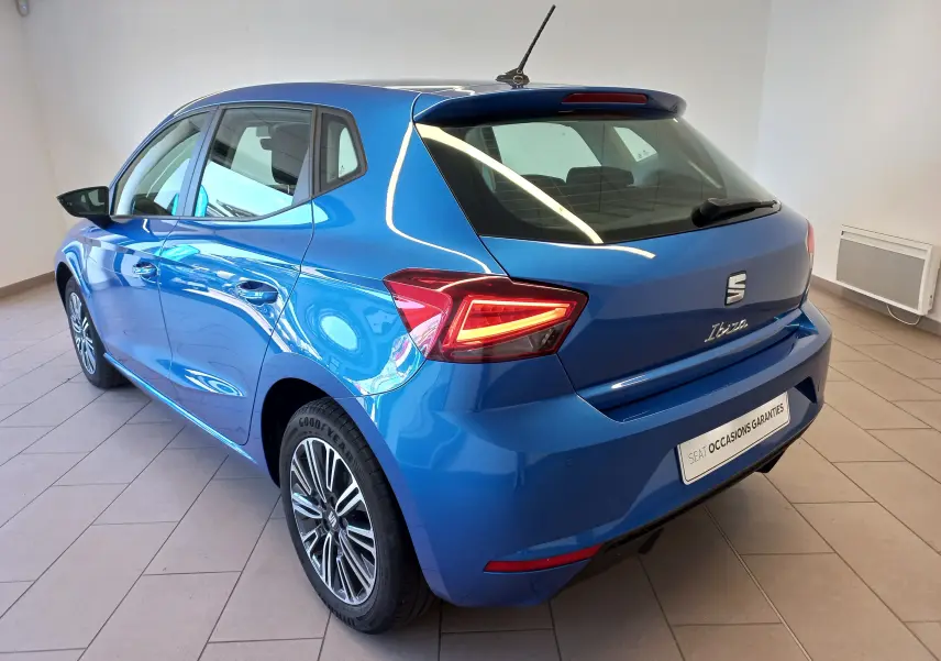 Vue 3/4 arrière droite d'une SEAT Ibiza 2025 bleu saphir avec feux arrière allumés et jantes alliage distinctives.