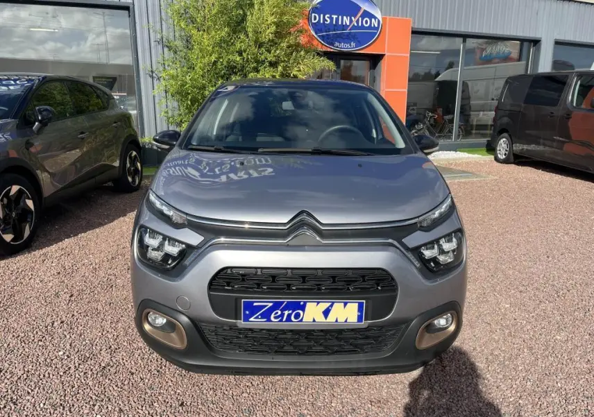 Vue frontale d'une Citroën C3 gris métallisé avec phares LED et plaque Zéro KM sur parking extérieur.