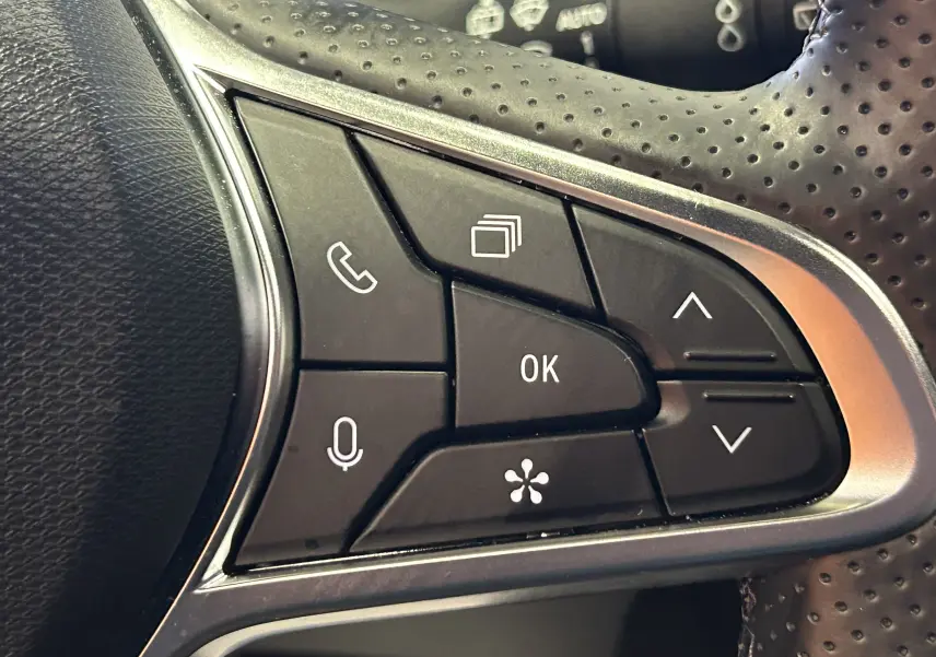 Gros plan sur les commandes multifonctions du volant perforé d'une Renault Symbioz blanc nacré, version hybride 2025.