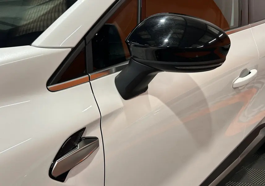 Gros plan sur la porte côté gauche d'une Renault Symbioz blanc nacré, avec rétroviseur noir brillant et poignée intégrée.