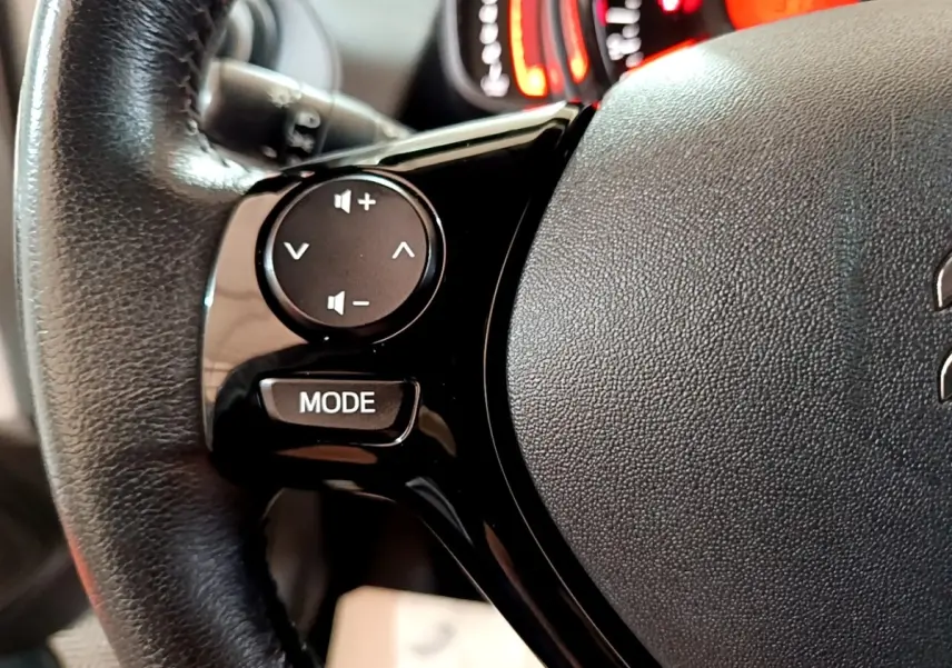 Gros plan sur les commandes du volant cuir noir de la Citroën C1 VTi 72 Shine, avec boutons de volume et mode.