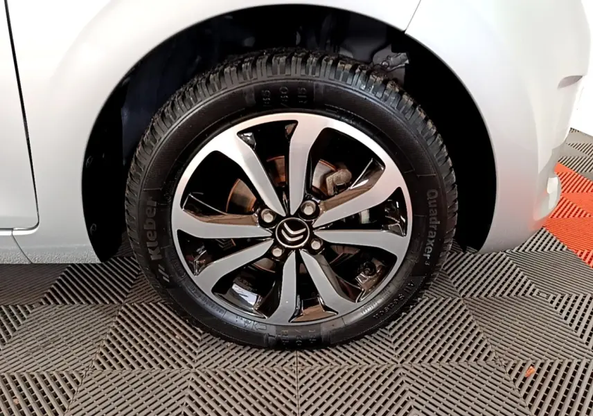 Gros plan sur la roue avant droite d'une Citroën C1 gris clair, mettant en valeur la jante alliage bicolore.