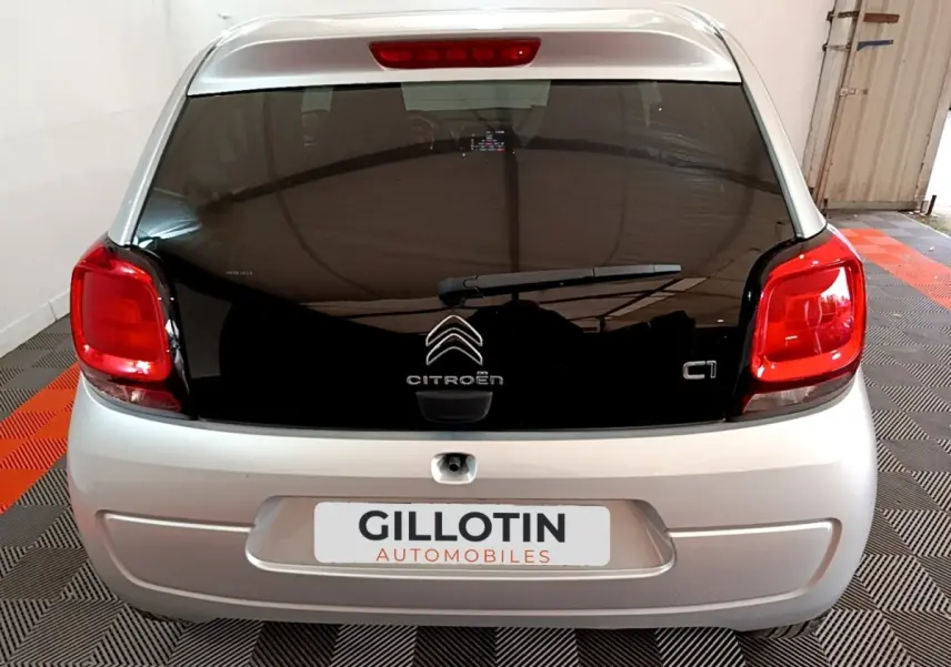 Vue arrière d’une Citroën C1 gris clair avec hayon noir et feux arrière rouges dans un garage.