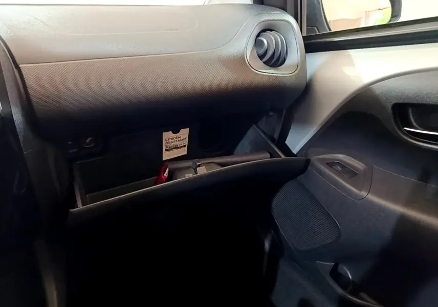 Intérieur côté passager d'une Citroën C1 gris clair 2019, boîte à gants ouverte avec ventilation ronde visible.