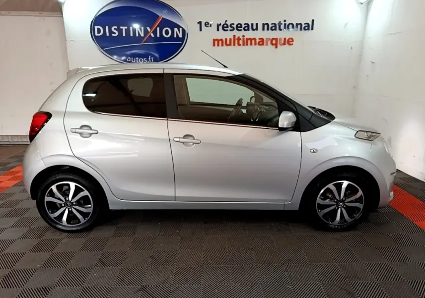 Profil droit d'une Citroën C1 gris clair 2019 avec jantes alliage noires et vitres teintées en intérieur showroom.