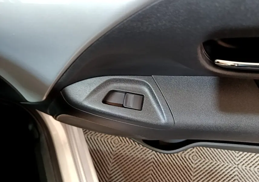 Gros plan sur la commande de réglage des rétroviseurs côté conducteur d’une Citroën C1 gris clair, intérieur noir.