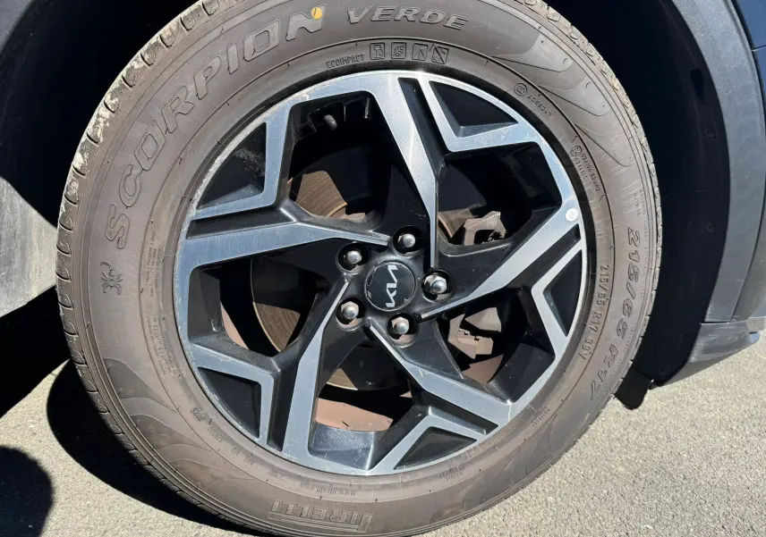 Gros plan sur la roue avant droite du Kia Sportage noir 2022, mettant en valeur la jante alliage noire et argentée avec logo Kia central.