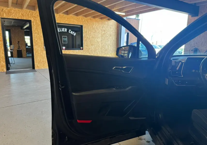 Vue intérieure côté gauche de la porte avant ouverte d’un KIA Sportage noir 2022, avec tableau de bord partiellement visible.