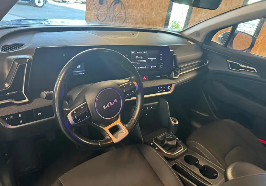 Vue intérieure côté conducteur du Kia Sportage noir 2022, volant cuir, tableau de bord numérique et boîte manuelle.