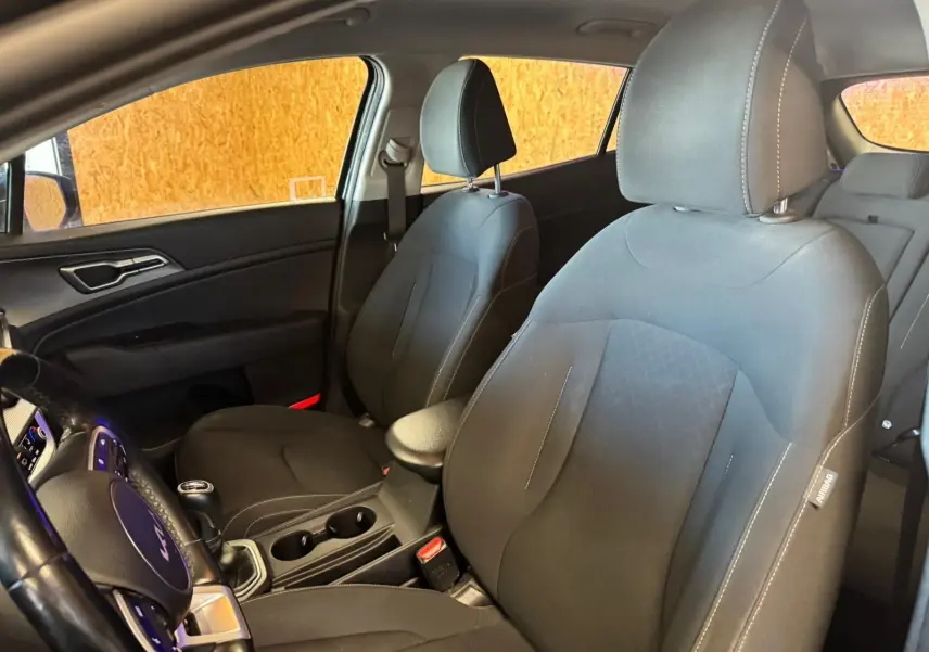 Vue intérieure côté conducteur du Kia Sportage 2022 noir, siège tissu noir avec coutures blanches et volant multifonction.