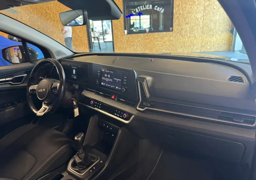 Intérieur noir du Kia Sportage 2022, vue côté conducteur sur tableau de bord moderne avec écran tactile et boîte manuelle.