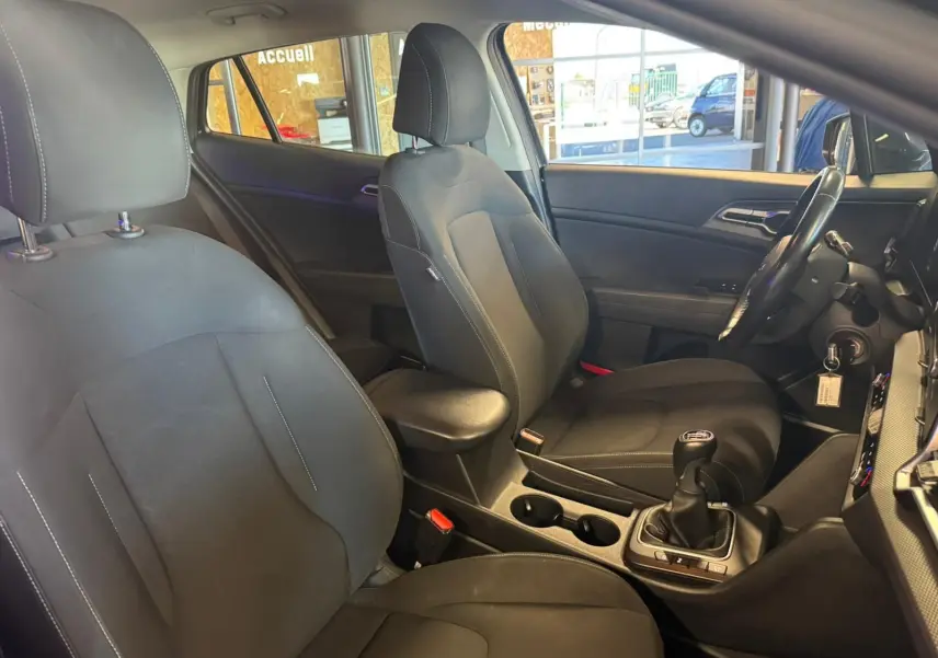 Vue intérieure côté conducteur du Kia Sportage noir 2022, mettant en valeur les sièges tissu noirs et la boîte manuelle.