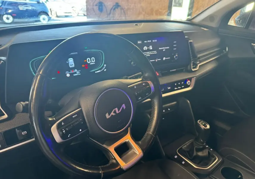 Vue intérieure côté conducteur du tableau de bord noir du Kia Sportage 2022 avec volant multifonction et boîte manuelle.