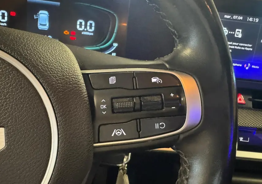 Gros plan sur le volant noir du KIA SPORTAGE 2022, montrant les commandes de régulateur de vitesse et tableau de bord digital.