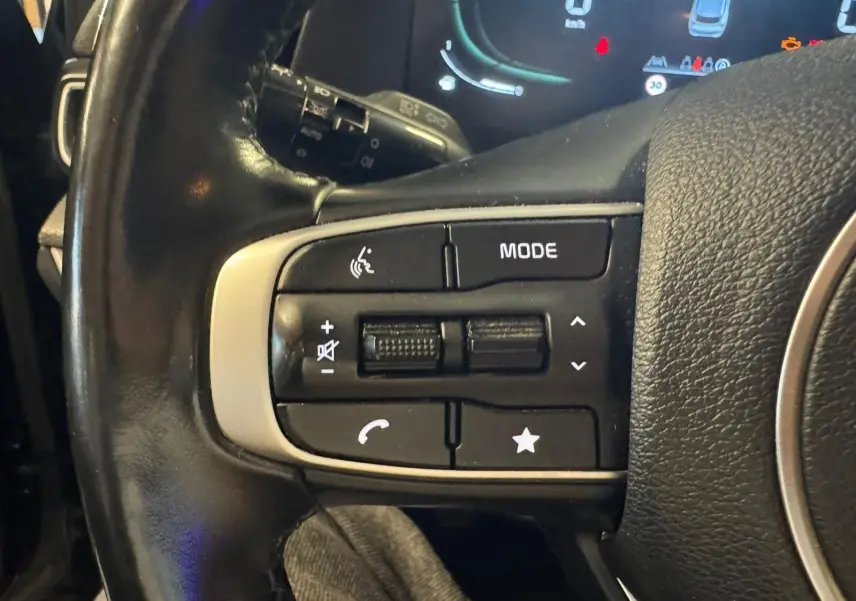 Gros plan sur les commandes gauche du volant noir du KIA SPORTAGE 2022, avec boutons de volume et mode audio visibles.