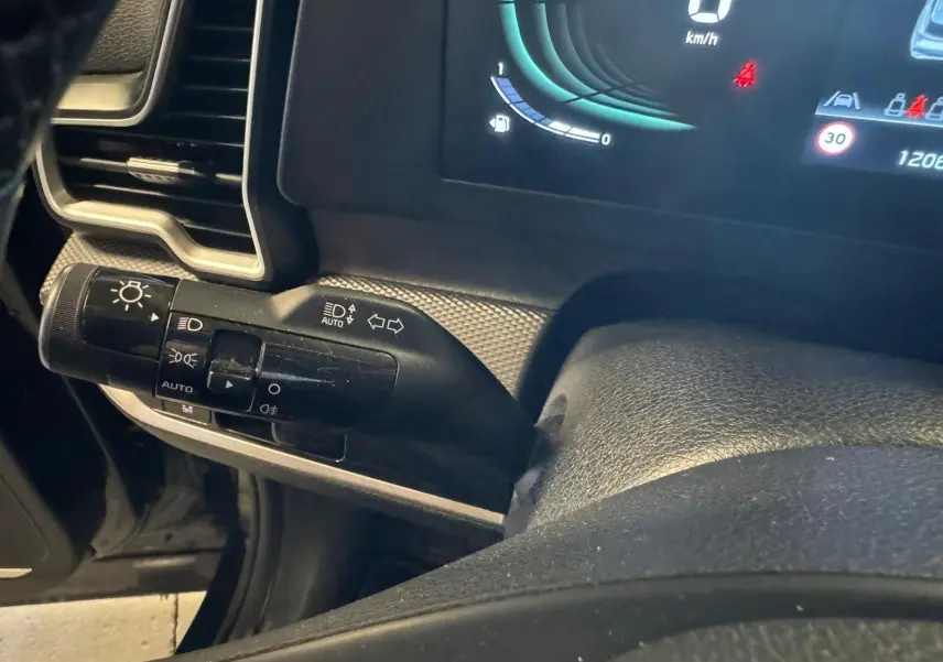 Gros plan sur la commande des phares et clignotants à gauche du volant du Kia Sportage noir, tableau de bord digital visible.