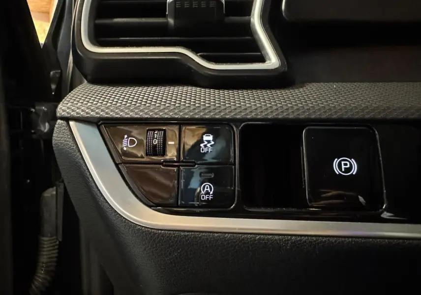 Détail des commandes côté gauche du tableau de bord du Kia Sportage noir 2022, avec boutons d'assistance et frein à main électronique.