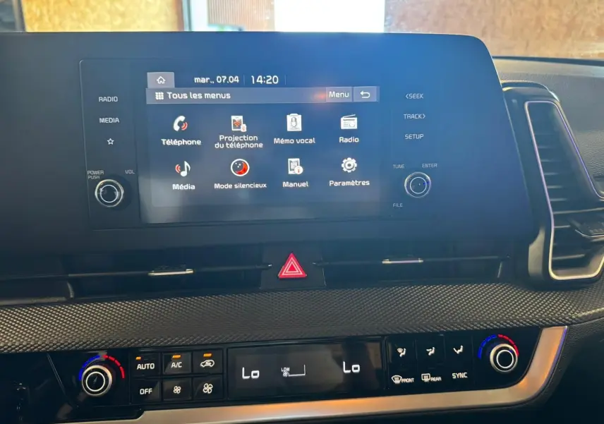 Vue rapprochée de l’écran tactile et de la console centrale du Kia Sportage noir, affichant les commandes multimédia et climatisation.