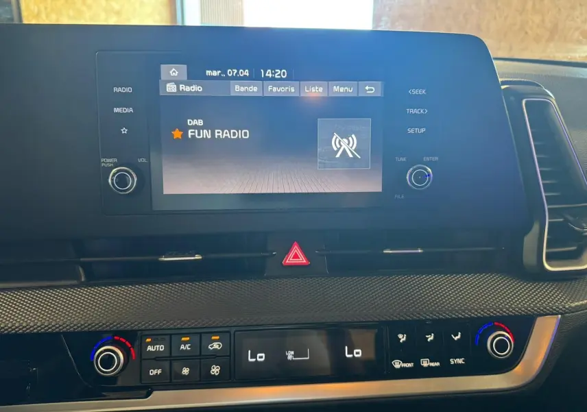 Vue rapprochée de l’écran multimédia et de la console de climatisation du Kia Sportage noir, affichant Fun Radio.