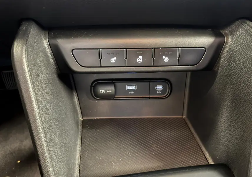 Vue rapprochée des commandes de sièges chauffants et des ports USB et 12V dans l’habitacle noir du Kia Sportage 2022.