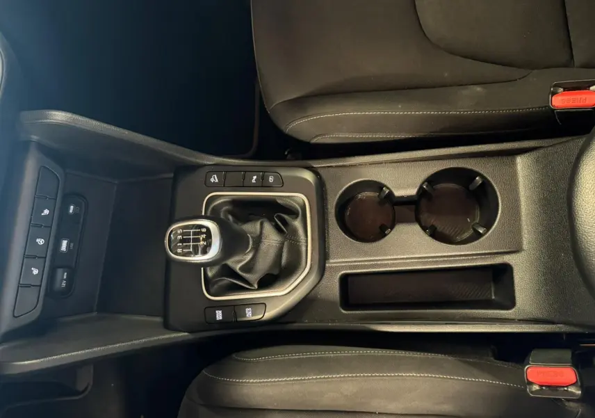Vue plongeante sur la console centrale noire du Kia Sportage 2022, avec levier de vitesse manuel et porte-gobelets.