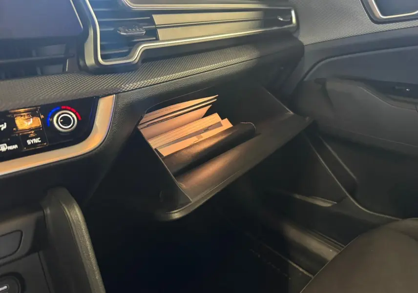 Intérieur noir du Kia Sportage 2022, vue côté passager sur la boîte à gants ouverte avec documents visibles.