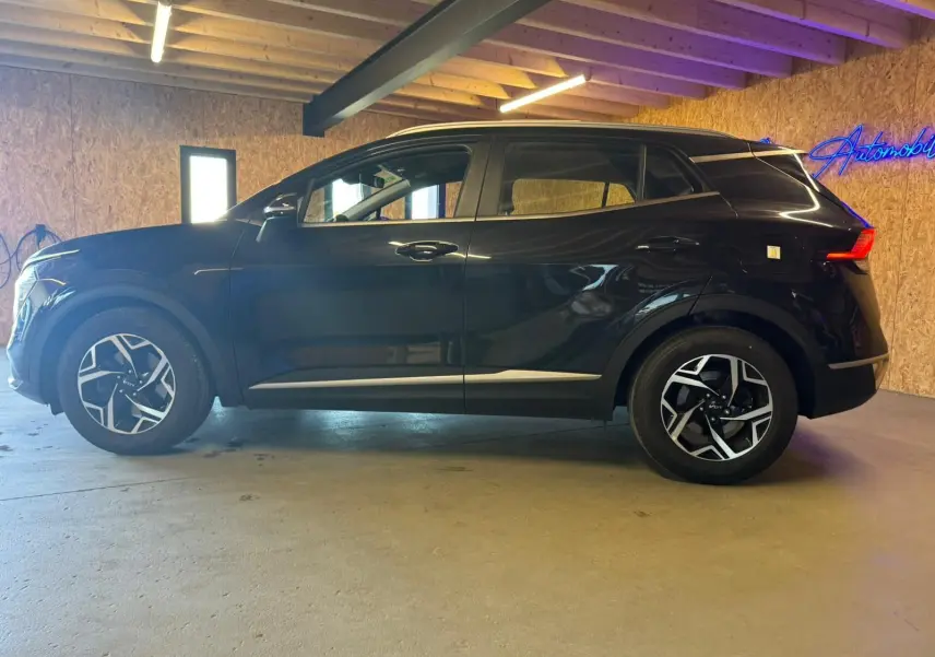 Vue latérale droite d'un KIA Sportage noir 2022, soulignant ses jantes alliage au design moderne dans un garage.