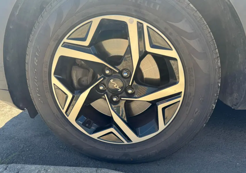 Gros plan sur la roue avant droite du Kia Sportage noir 2022, mettant en valeur la jante alliage bicolore et le pneu Pirelli.