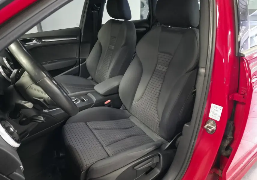 Vue intérieure côté conducteur de l'Audi A3 Sportback rouge, montrant les sièges avant en tissu et cuir noir.