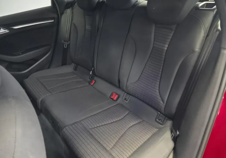 Vue intérieure arrière des sièges en tissu noir de l'Audi A3 Sportback rouge, avec ceinture de sécurité visible côté droit.