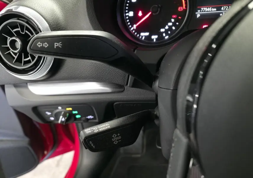 Gros plan sur les commandes de volant et tableau de bord d'une Audi A3 Sportback rouge, avec compte-tours et affichage digital.