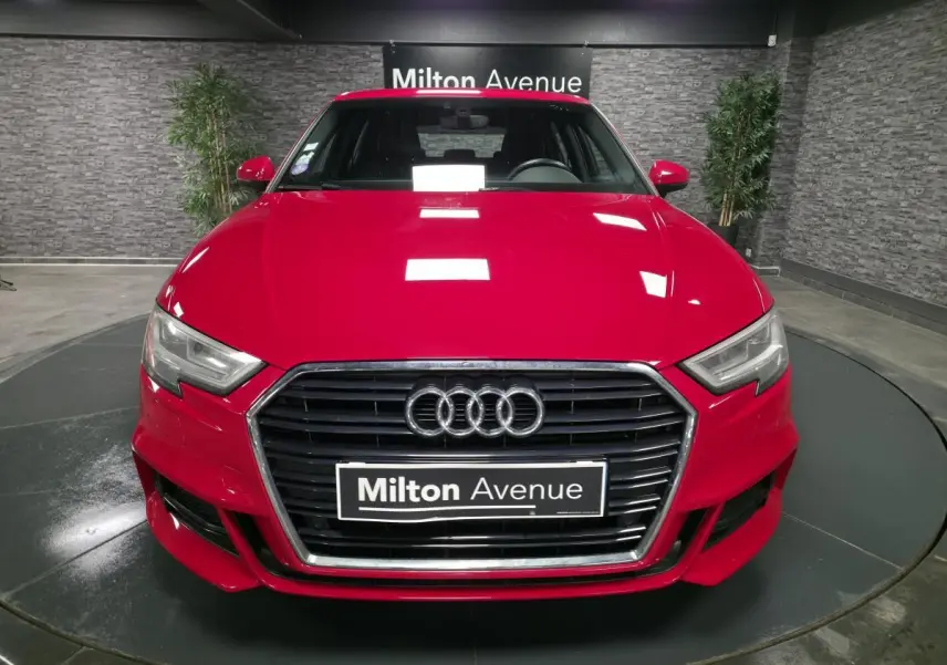 Vue avant d'une Audi A3 Sportback rouge avec calandre noire et logo Audi, en intérieur showroom.
