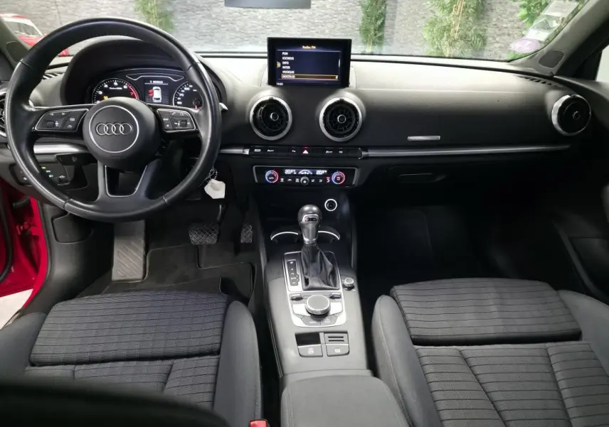 Vue intérieure avant de l'Audi A3 Sportback 2019, tableau de bord noir avec volant multifonction et écran central.