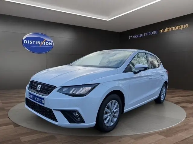 Vue 3/4 avant droite d'une SEAT Ibiza blanche 2023 avec vitres arrière surteintées et feux LED, en showroom.