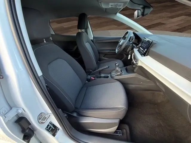 Vue intérieure côté conducteur d'une SEAT Ibiza blanche 2023, montrant les sièges avant, le volant cuir multifonctions et l'écran tactile central.