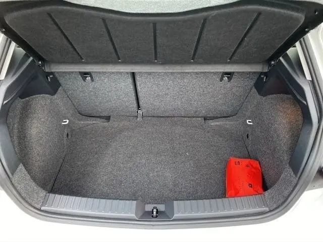 Coffre ouvert vu de l'arrière d'une SEAT Ibiza blanche 2023, avec tapis gris et trousse de secours rouge visible.