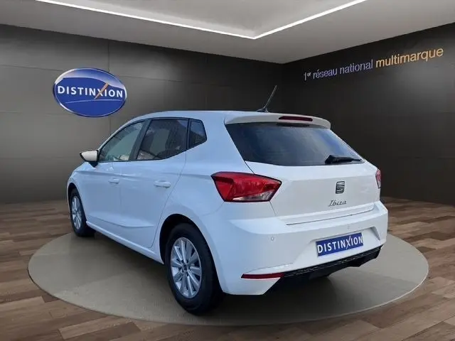 Vue 3/4 arrière gauche d'une SEAT Ibiza blanche 2023 avec vitres arrière surteintées dans un showroom.