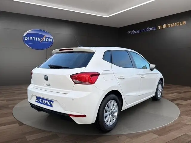 Vue 3/4 arrière droite d'une SEAT Ibiza blanche 2023 avec vitres arrière surteintées dans un showroom.
