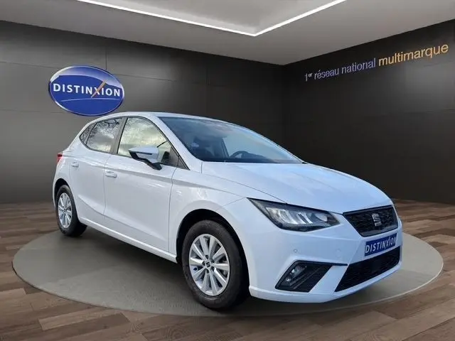 Vue 3/4 avant droite d'une SEAT Ibiza blanche 2023 avec vitres arrière surteintées dans un showroom.