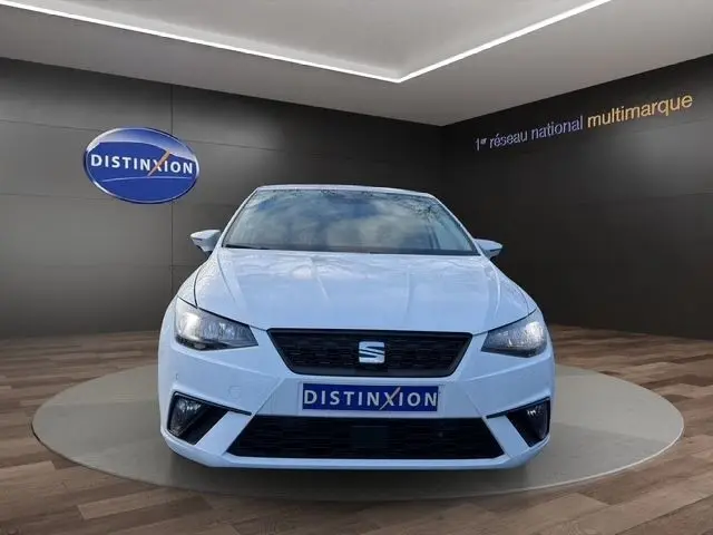 Vue de face d'une SEAT Ibiza blanche 2023 avec vitres arrière surteintées et feux LED, exposée en showroom.