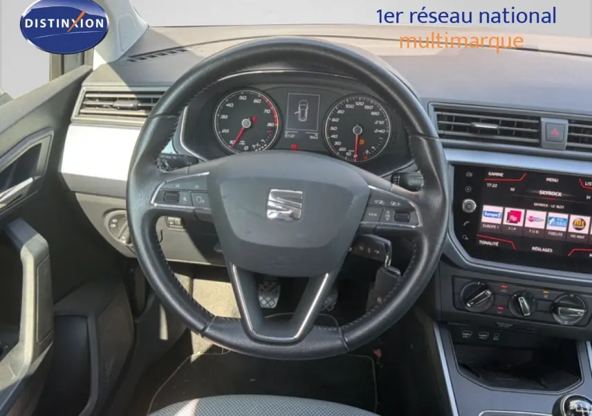 Vue intérieure centrée sur le volant et le tableau de bord d'une SEAT Arona gris urbain avec écran tactile et commandes au volant.