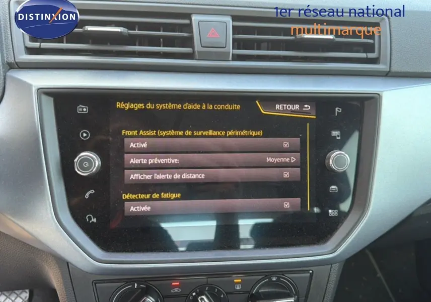 Vue rapprochée de l’écran tactile central du tableau de bord du SEAT Arona gris urbain avec toit noir, affichant les réglages d’aide à la conduite.