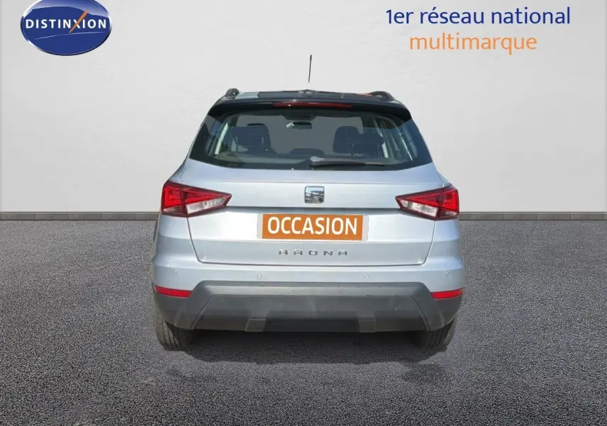 Vue arrière d'un SEAT Arona gris urbain avec toit noir, immatriculé occasion, en extérieur sur sol goudronné.