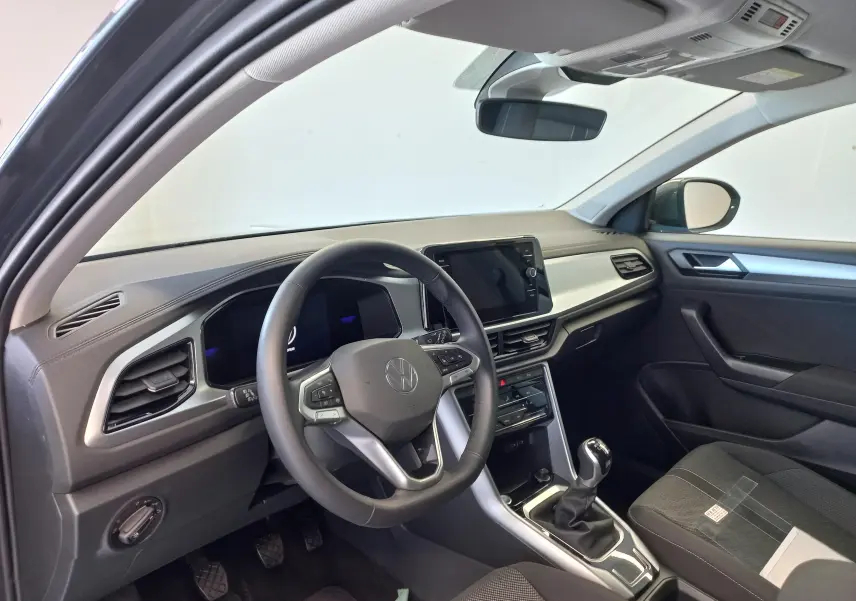 Vue intérieure côté conducteur du Volkswagen T-Roc 2025, tableau de bord moderne avec volant multifonction et levier de vitesse manuel.