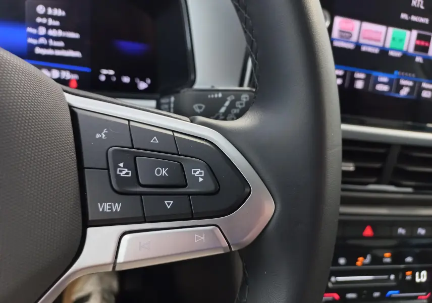 Gros plan sur les commandes au volant côté gauche du Volkswagen T-Roc 2025, avec écran digital en arrière-plan flou.